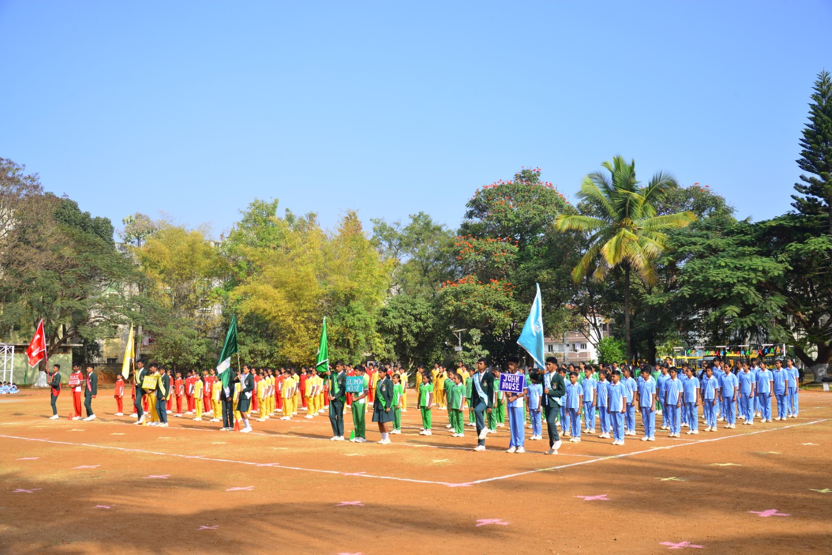 A group of students in sports uniforms marching in formation during Bethesda International School's Sports Day event, with flags waving in the background